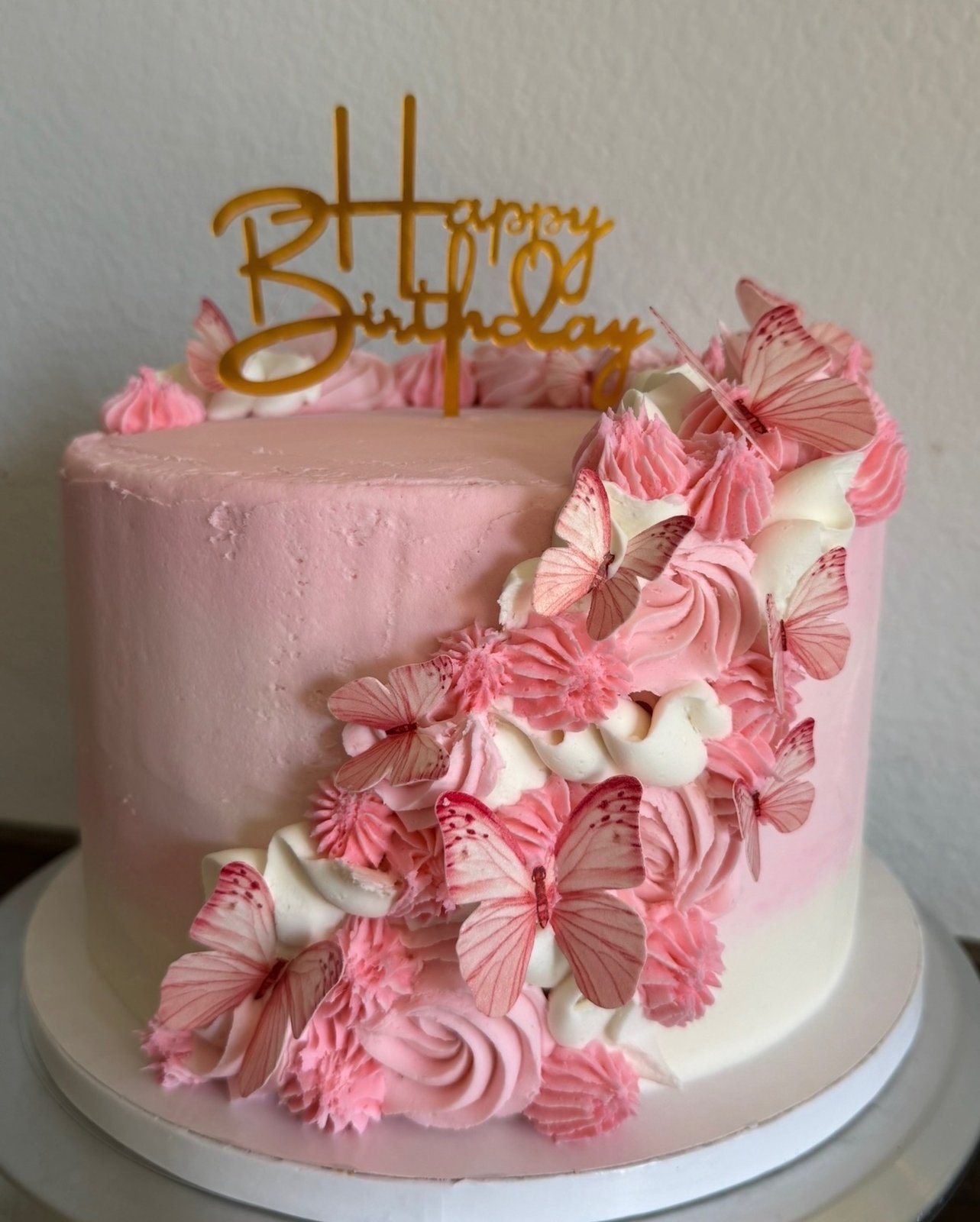 Pink birthday cake with piped buttercream flowers and a gold Happy Birthday topper